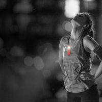A young woman catching her breath after a running session, using the SwivelClip to light the way during an evening run.